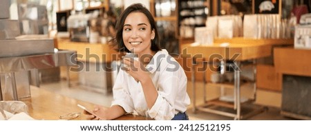 Portrait of beautiful asian woman with smartphone, relaxing in cafe, sitting and enjoying coffee while using mobile phone.