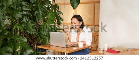 Excited asian girl found something online, looking at laptop screen with surprised, amazed face, sitting in cafe.