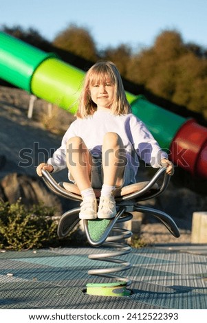A cute blonde girl is sitting on a swing in the playground. The concept of a happy childhood.