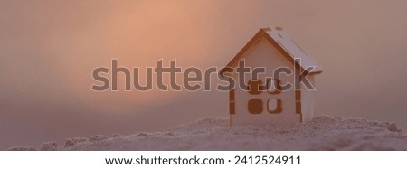 Toy house on the sandy beach in the red summer sunset. Panoramic image. Defocused sun disk and blurred sky as background. Abstraction. Conceptual. Sense of openness, warmth and hospitality