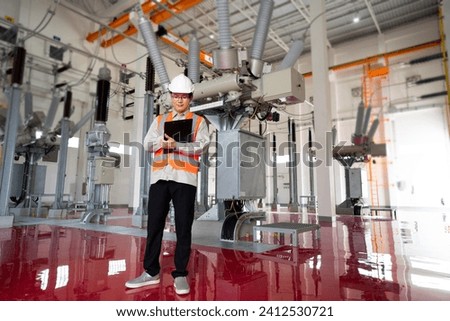 Asian engineer in safety uniform with record paper at powerhouse interior building. Royalty-Free Stock Photo #2412530721