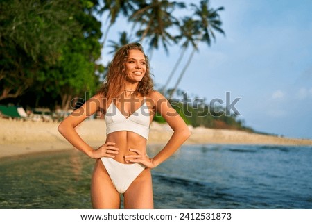 Fit solo female traveler enjoys serene tropical beach journey. Independent woman in swimwear explores sandy shore alone. Adventure, travel, wellness, and self-love concept in nature.