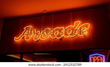 A glowing neon sign with the word "Arcade" illuminated in bright blue and yellow colors, displayed outside a restaurant called Arcade