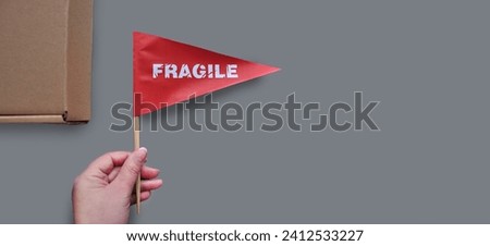 Small paper flags in hand with the warning 'Fragile' as a label. The concept of fragile products. Monochrome gray background. Copy space