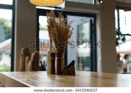 Photography of the cafe interior.  Napkin stand, pepper shaker, salt shaker, jar of seasonings. Bouquet of dry wheat stalks as decoration. Bokeh