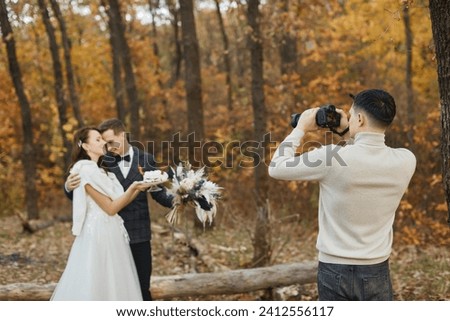 male wedding photographer taking pictures of the bride and groom in nature in autumn