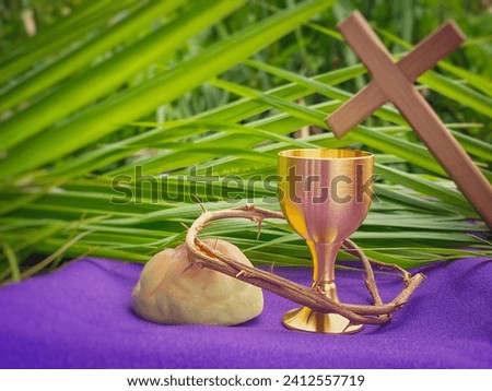 Holy Week, Lent, Palm Sunday, Maundy Thursday, Good Friday, Easter Sunday Concept. Chalice, Crown of thorns, bread and palm leaf with purple background. Royalty-Free Stock Photo #2412557719