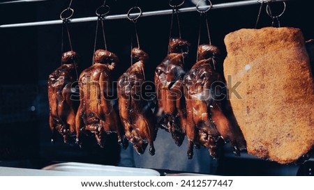 Roasted crispy ducks hanging from metal meat hooks in the window of a chinese restaurant