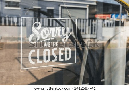 Sorry we're closed " sign in black and white, on shop glass door