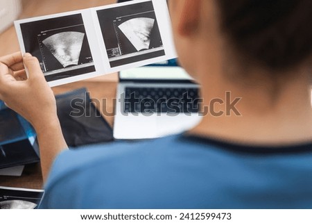 Therapist in blue medical uniform looks at results of ultrasound examination closeup doctor studies information to establish diagnosis and prescribe treatment backside view