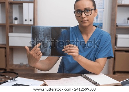 Woman traumatologist points finger at X-ray picture talking to patient online looking at camera doctor consults visitor remotely treatment in modern clinic