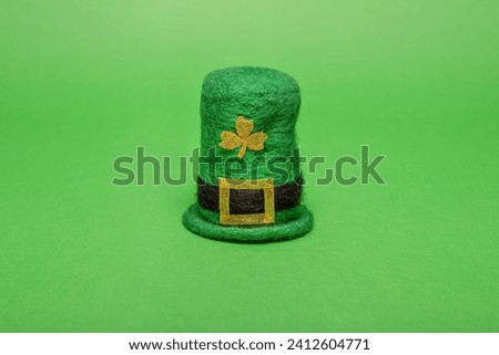 On a green isolated background Leprechaun hat for St. Patricks Day. Minimalist decor, greeting card to the Irish tradition. Golden trefoil for good luck. Copy space, mock up