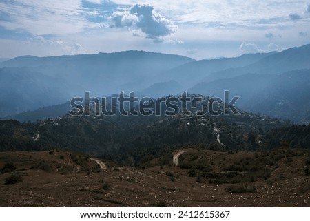 An aerial view of a mountain range covered in white mist and deciduous forest under a cloudy sky on a warm day.