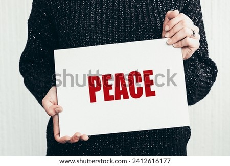close up of a Protester hands holding cardboard Banner with the words peace. protesting against the Russian invasion. Royalty-Free Stock Photo #2412616177