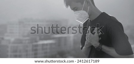 A sick young man wears a mask to protect against PM 2.5 dust coming from the city and air pollution. Haze, dust and smog with bad weather. Pollution, Covid, bad weather Royalty-Free Stock Photo #2412617189