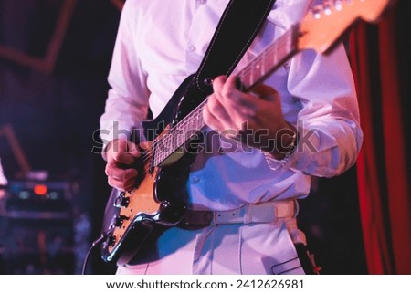 Concert view of an electric guitar player with vocalist and rock band performing in a club, male musician guitarist on stage with audience in a crowded concert hall arena
