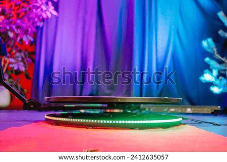 360-degree photo booth platform on a red carpet with a colorful backdrop, including a blue curtain and a plant.