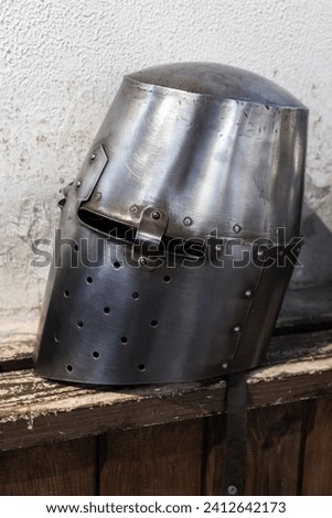 Closed steel helmet of medieval knight lays on a rough wooden shelf  in front of white wall