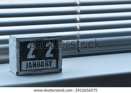 Morning January 22 on wooden calendar standing on window with blinds