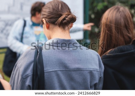 Group of students and school pupils on outdoor excursion tour in the city streets with guide, a docent with a tourist adult visitors, school field trip, urban tour in the summer sunny day Royalty-Free Stock Photo #2412666829
