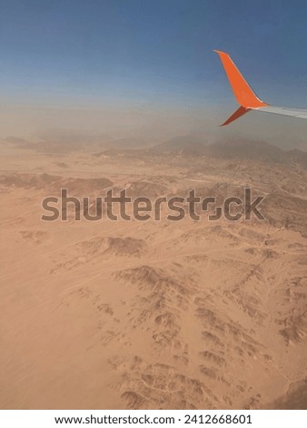 A photo of the airplane wing with the orange winglet during the flight above the desert Royalty-Free Stock Photo #2412668601
