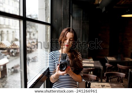 Young woman photographer with old 6x6 frame camera standing near the big window in the cafe