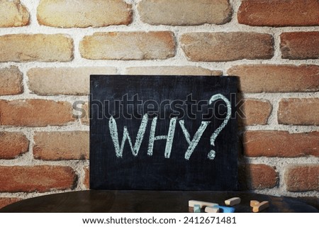 Black board with the word WHY? drown by hand on wooden table on brick wall background. For business presentation.