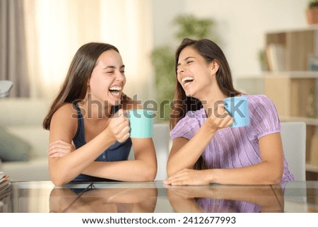 Two happy friends drinking and laughing hilariously at home Royalty-Free Stock Photo #2412677993