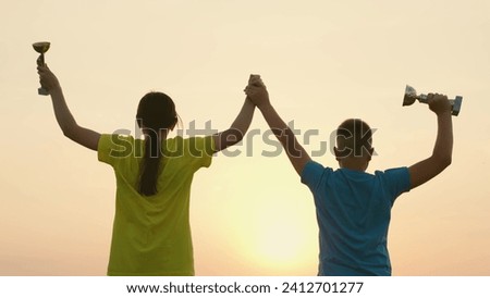 Teenagers won team competition. Celebrating the team victory, winners with cups in their hands rejoice and jump. Silhouette happy athletes champions in sports man and woman teamwork. Slow motion Royalty-Free Stock Photo #2412701277