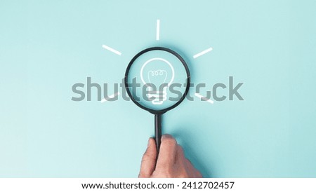 Exploring innovation Ideas and creativity concept with light bulb icon through magnifying glass holding in hand in pastel blue background. Royalty-Free Stock Photo #2412702457