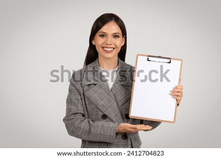 Professional woman in houndstooth blazer displaying blank clipboard, perfect for marketing messages or custom content, on grey background