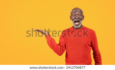 Happy shocked senior african american man with beard, open mouth, hold on hand copy space, isolated on orange studio background, panorama. Recommendation ad and offer, huge sale attention