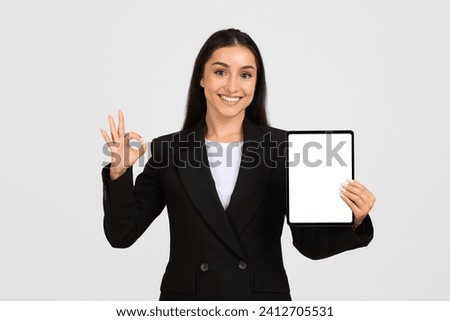 Portrait of smiling european businesswoman holding blank digital tablet screen and showing ok sign posing isolated over grey background, mockup