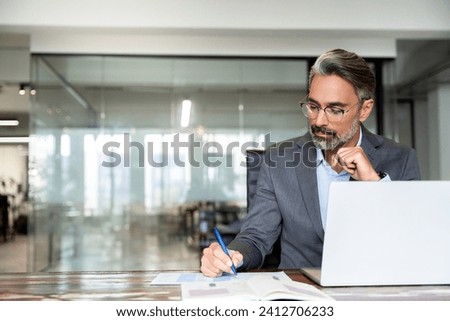 Middle-age Hispanic man using laptop computer for business studying, watch online virtual webinar training meeting, video call. Focused mature Indian or Latin businessman work in office, copy space. Royalty-Free Stock Photo #2412706233