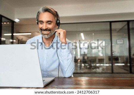 Happy senior latin Hispanic man in wearing headphones, helping as callcenter consult assistant. Smiling mature 40s years old mixed race businessman holding video call with clients partners. Copy space Royalty-Free Stock Photo #2412706317