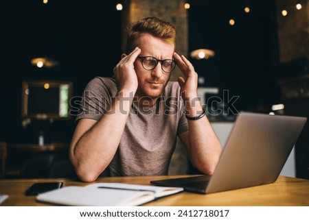 Unhappy Caucasian male blogger feeling headache during deadline job working on laptop computer, puzzled IT professional with netbook for programming solving overtime problems with graphic design