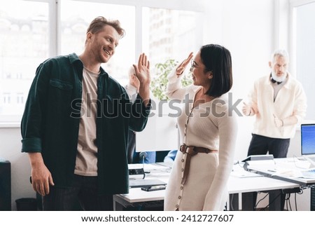Joyful male and female creative coworkers rejoicing with new startup idea making high five gesture during working day in modern office interior, cheerful employees enjoying business lifestyle Royalty-Free Stock Photo #2412727607