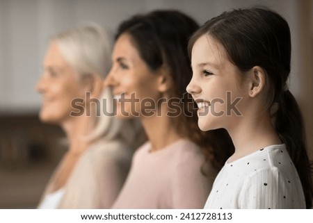 Happy pretty little tween girl standing by mother and grandma in line, looking away, smiling, laughing, posing for family side portrait. Three female family generations home shot