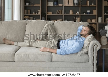 Side view man enjoy daytime nap on comfy sofa. Peaceful guy take break lying, sleeping on comfortable couch, rest in cozy living room, breath fresh conditioned air, relieving fatigue in modern flat Royalty-Free Stock Photo #2412728437