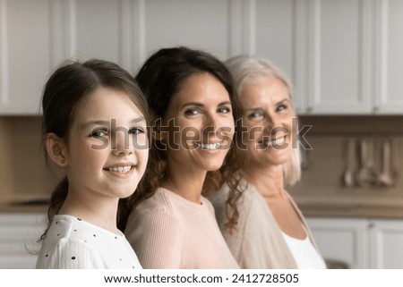 Happy cute little tween child girl, brunette mom and cheerful grandma posing for family shooting, standing in line, turning faces, heads to camera, smiling. Three female generations portrait