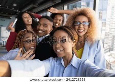 Office selfie. Friendly young biracial workers colleagues have fun at workplace shoot cute silly self picture on phone. Active millennial black business team take funny group photo for corporate blog