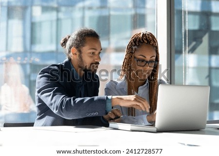 Internship. Confident black man mentor coach help teach explain work on project to biracial woman intern at workplace. Two young diverse mixed race colleagues share ideas interacting by laptop screen Royalty-Free Stock Photo #2412728577