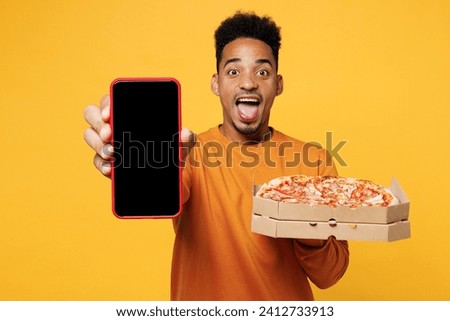 Young man wear casual clothes hold italian pizza in cardboard flatbox use black screen mobile cell phone isolated on plain yellow background Proper nutrition healthy fast food unhealthy choice concept Royalty-Free Stock Photo #2412733913