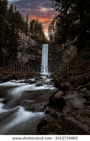 A fine art landscape photography image of Brandywine Falls in Whistler British Columbia Canada during a colourful and dynamic sunset over the flowing falls and dreamy river in the foreground
