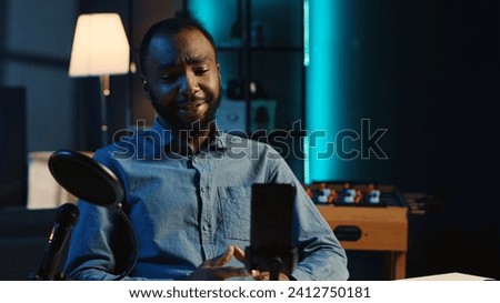 Content creator arriving in dimly lit studio, using smartphone camera to record video intro for online streaming platforms. Influencer greets fanbase, using mobile phone to capture footage Royalty-Free Stock Photo #2412750181