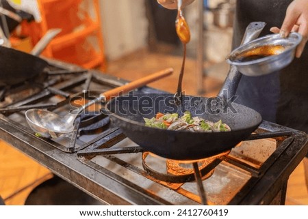 Close-up photo of a chef adding sauce to mixed vegetables in a frying pan