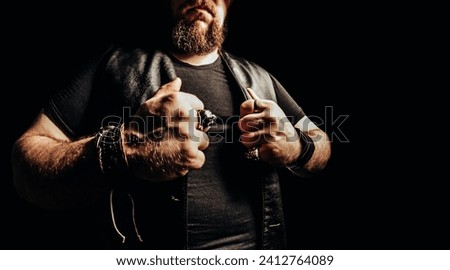 Photo of a shaded male muscular bearded biker putting on leather vest. Royalty-Free Stock Photo #2412764089