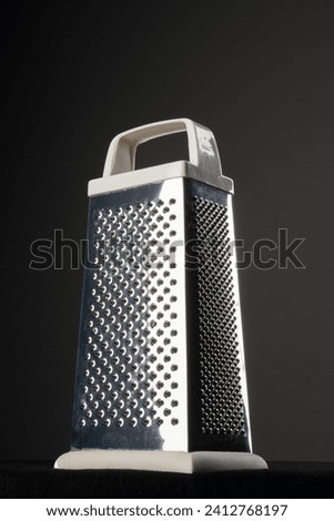 silver grater with white handle illuminated with a side light