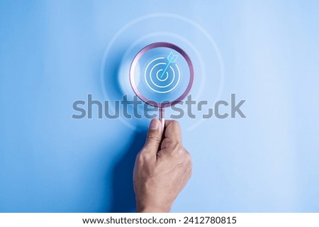 achievement, business, goal, strategy, target, accuracy, focus, achieve, aim, management. hand holding target board inside magnifying glass for focus business on blue background. search, goal.