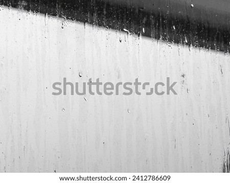 Raindrops and rain streaks on a residential window near a dark ledge of concrete on a gray morning in Florida, in black and white, for motifs of transparency, weather, prospects and decisions Royalty-Free Stock Photo #2412786609